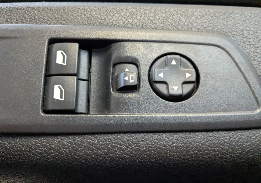 Gros plan sur les commandes noires de réglage des rétroviseurs et des vitres sur la porte intérieure d’un Opel Vivaro Fourgon blanc.
