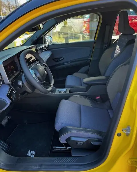 Vue intérieure côté conducteur de la Renault R5 Techno jaune 2024, sièges tissu gris et tableau de bord digital.