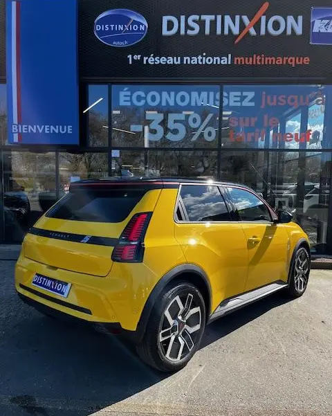 Vue 3/4 arrière droite d'une Renault R5 Techno jaune électrique stationnée devant une vitrine avec enseigne Distinxion.