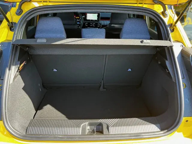 Vue arrière du coffre ouvert d'une Renault R5 jaune 2024, avec intérieur noir et écran tactile visible à l'avant.