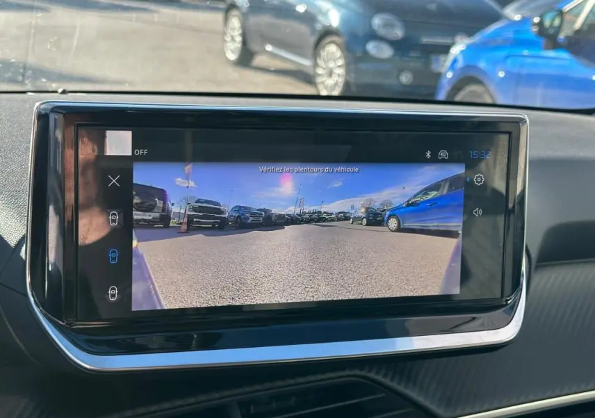 Écran tactile intérieur montrant la caméra de recul d'une Peugeot 208 Hybrid 110 gris, vue depuis le tableau de bord.