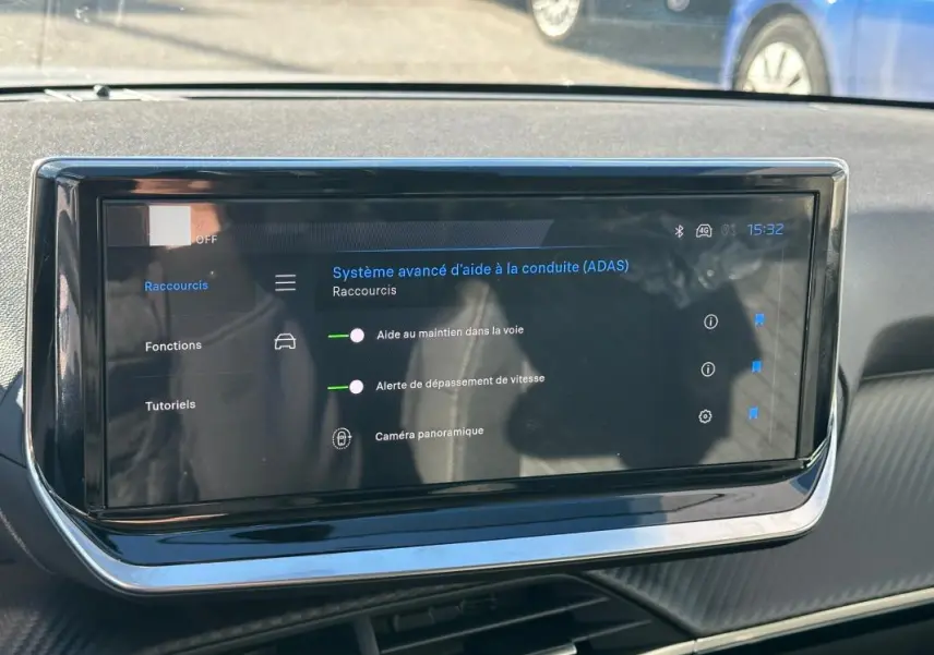 Écran tactile central du tableau de bord d’une Peugeot 208 gris, affichant les aides à la conduite.