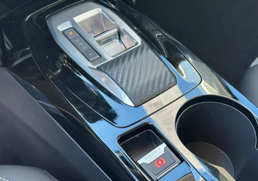 Gros plan sur la console centrale noire brillante de la Peugeot 208 Hybrid 110, avec levier de boîte auto et frein à main électrique.