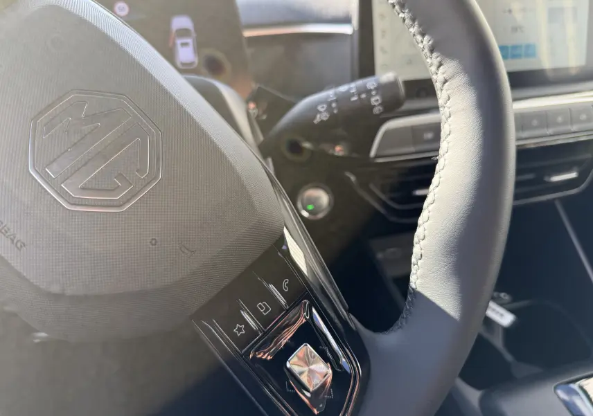 Gros plan sur le volant noir cuir de la MG3 1.5 HYBRID+ 195 LUXURY avec commandes tactiles et tableau de bord numérique flou.