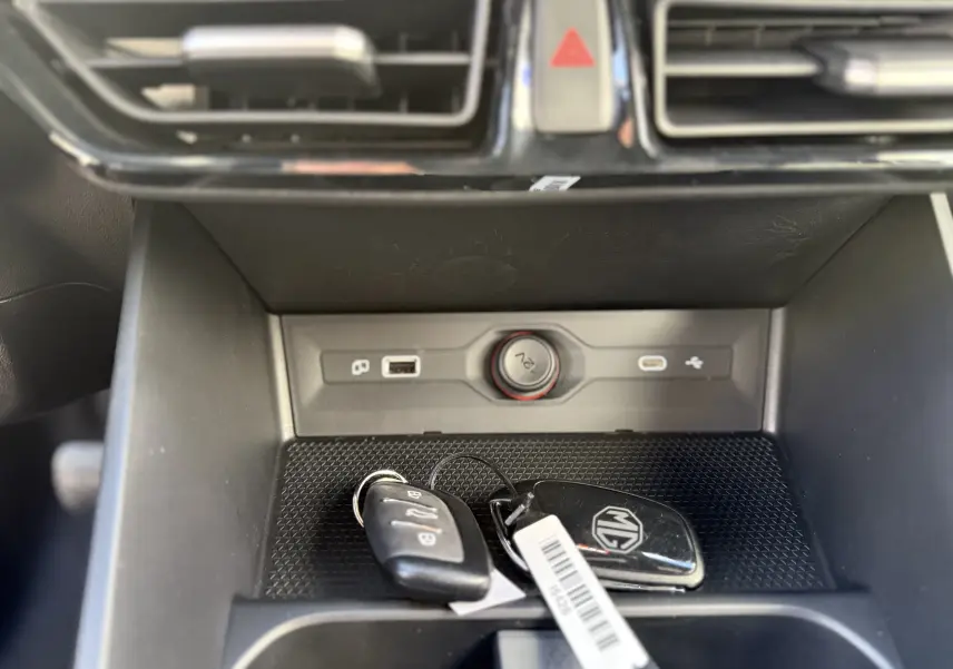 Gros plan intérieur sur la console centrale noire avec clés MG posées, prise 12V et ports USB visibles.