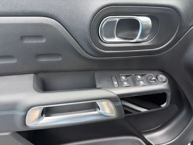 Détail de la porte côté conducteur de la Citroën C5 hybride gris clair 2024, avec commandes électriques et poignée argentée.