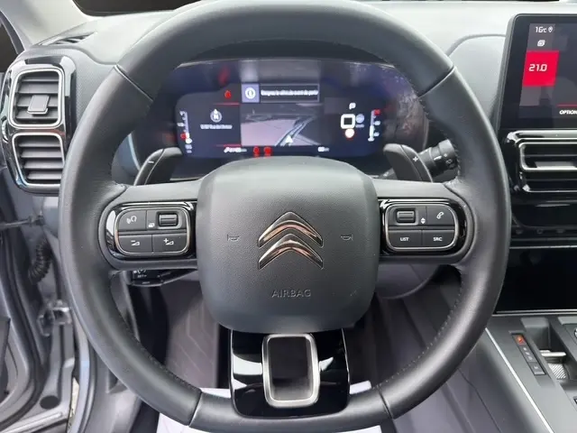 Vue rapprochée du volant cuir multifonctions noir de la Citroën C5 Hybride 2024 avec tableau de bord numérique et écran tactile.
