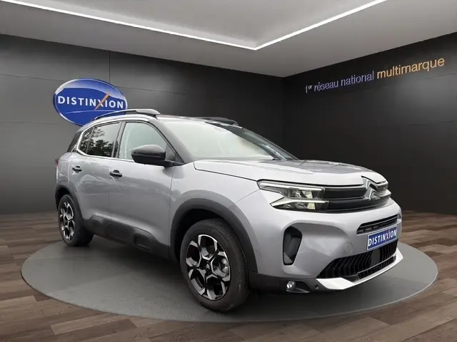 Vue 3/4 avant d'un Citroën C5 Hybride gris clair avec jantes noires et toit noir dans un showroom.