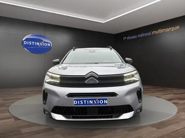Vue frontale d'une Citroën C5 hybride gris clair avec calandre noire et éclairage LED distinctif en showroom.