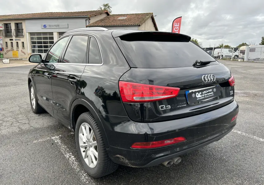 Audi Q3 noir vue 3/4 arrière droit, avec feux rouges et jantes argentées, stationné sur un parking extérieur.