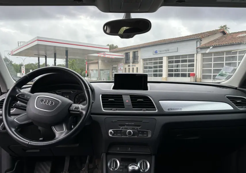 Intérieur noir de l'Audi Q3 2014, vue du tableau de bord et volant avec écran central et commandes climatisation.