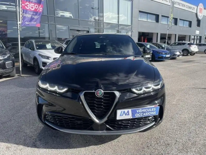 Vue de face de l'Alfa Romeo Tonale noire 2023 avec calandre triangulaire et phares LED allumés sur parking.