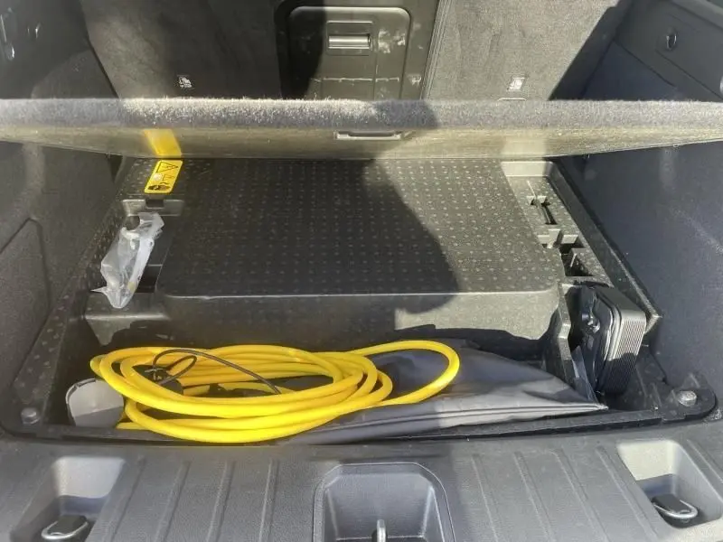 Coffre ouvert d'Alfa Romeo Tonale noir 2023 montrant le rangement sous plancher avec câble de recharge jaune visible.