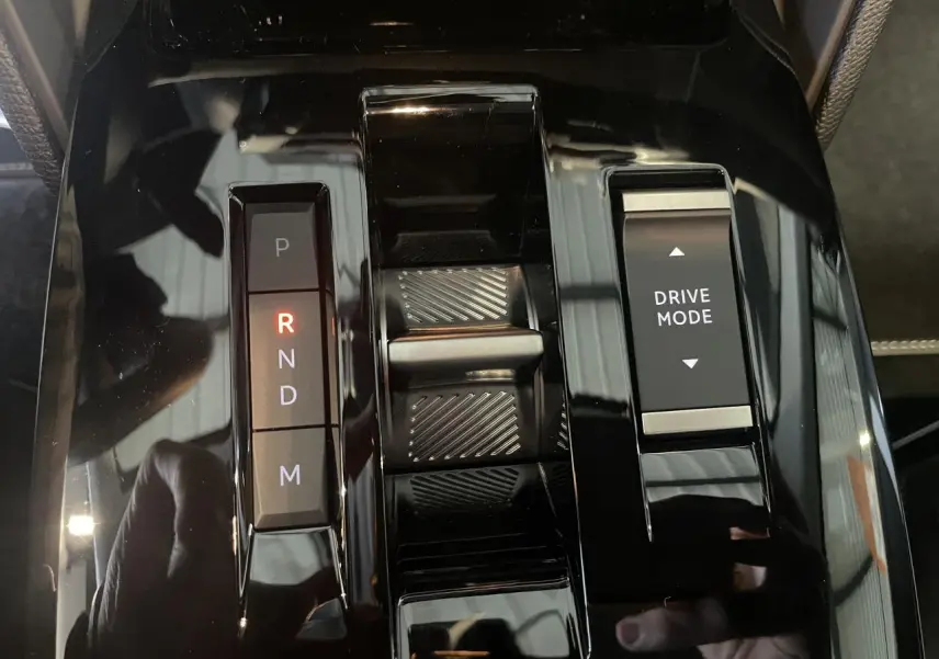 Gros plan sur la console centrale noire brillante de la Citroën C4 hybride avec sélecteur de boîte automatique et bouton Drive Mode.