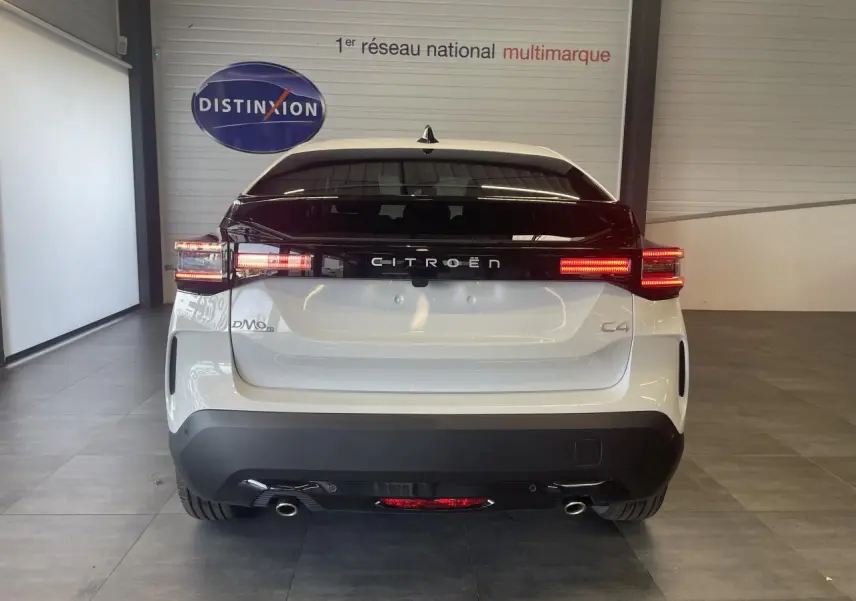 Vue arrière d'une Citroën C4 blanche métallisée avec feux LED allumés et bande noire distinctive sur le coffre.