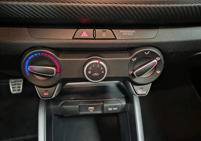Vue rapprochée de la console centrale de la Kia Rio rouge 2022, montrant les commandes de climatisation manuelle et prises USB/12V.