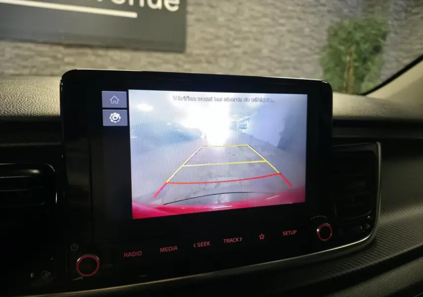 Écran tactile intérieur affichant la caméra de recul d'une Kia Rio rouge, vue du tableau de bord.