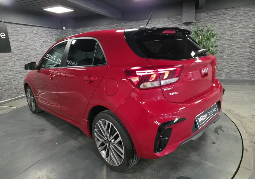 Vue 3/4 arrière droite d'une KIA Rio rouge métallisée GT Line avec jantes alliage et becquet noir laqué.