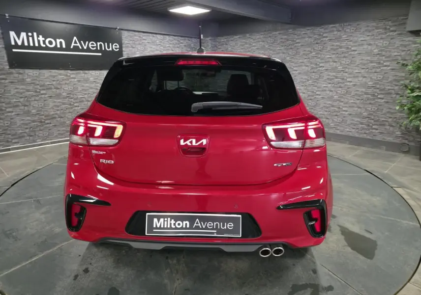 Vue arrière d'une KIA Rio GT Line rouge métallisée avec double sortie d'échappement et feux LED allumés.