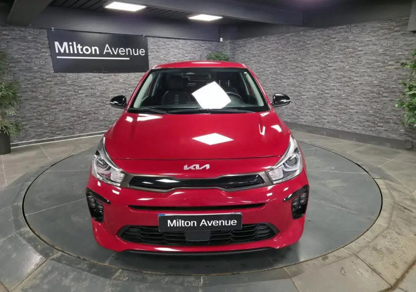 Vue avant d'une KIA Rio rouge métallisée GT Line 2022 avec calandre noire et phares LED dans un showroom.