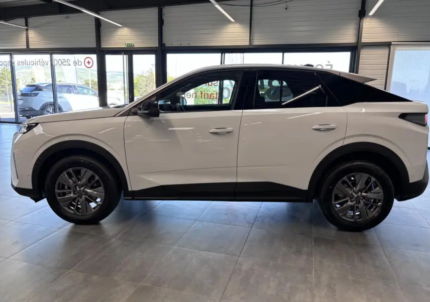 Vue de profil côté gauche d'un Peugeot 3008 blanc avec toit noir et jantes alliage 18 pouces en intérieur de showroom.