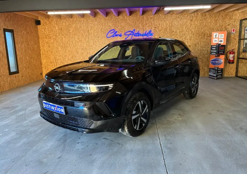 Opel Mokka 1.2 Turbo 145 Edition noir, vue 3/4 avant droit en intérieur avec éclairage naturel et néon bleu.