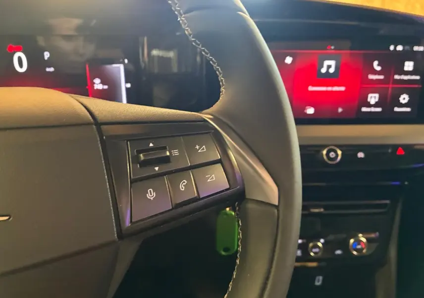 Vue intérieure du tableau de bord et volant noir de l'Opel Mokka 2025, avec commandes audio et écran tactile rouge en arrière-plan.