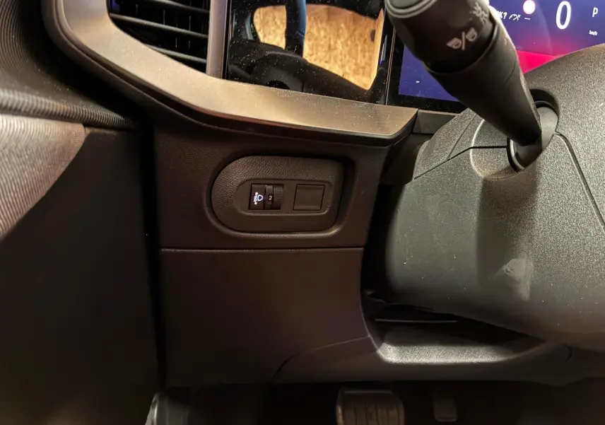 Détail intérieur côté gauche du tableau de bord noir de l’Opel Mokka 2025 avec commande de réglage des phares.
