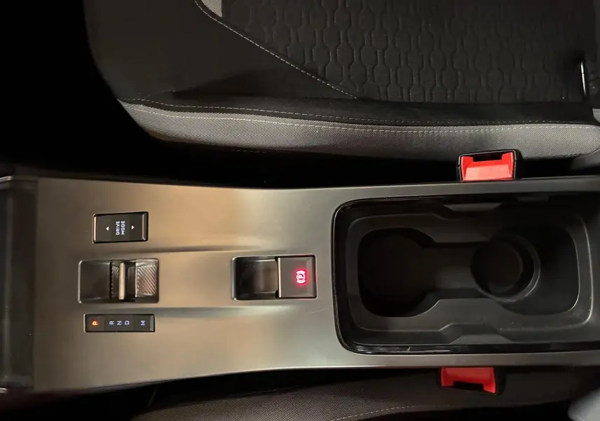 Vue plongeante sur la console centrale noire de l'Opel Mokka 2025, avec levier de boîte auto et bouton frein à main électrique allumé.