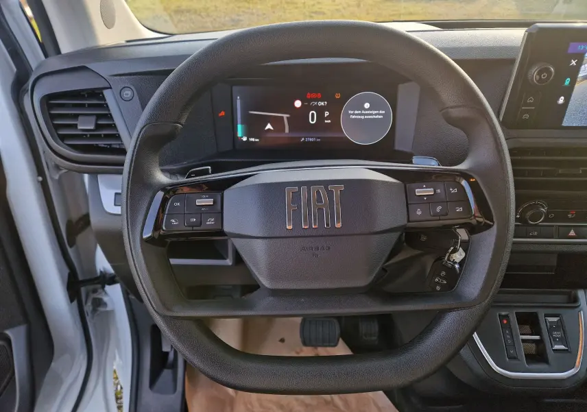 Vue rapprochée du volant noir avec logo FIAT et tableau de bord numérique du Fiat Scudo Fourgon blanc 2024.