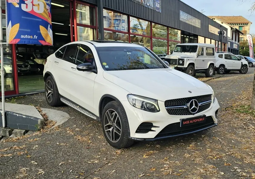 Mercedes GLC 220 Coupé blanc en 3/4 avant droit, avec calandre diamant et jantes alliage foncé, stationné devant un garage.