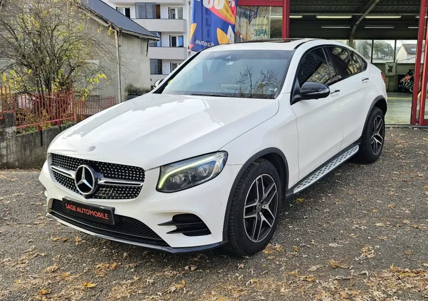 Vue 3/4 avant d'un Mercedes GLC 220 Coupé blanc avec jantes noires et calandre étoilée brillante.