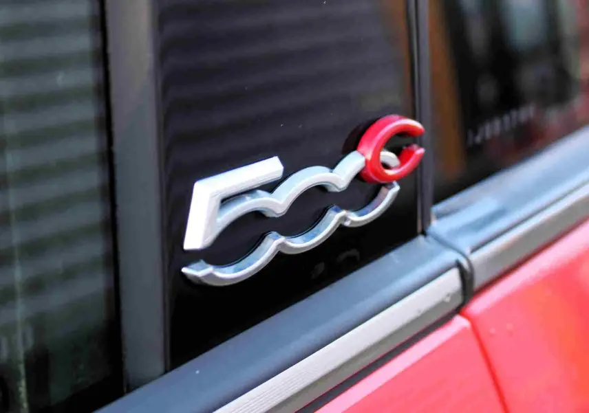 Vue 3/4 arrière droite d'une Fiat 500C 2018 rouge Pastel Coral avec toit ouvrant replié et jantes multibranches.