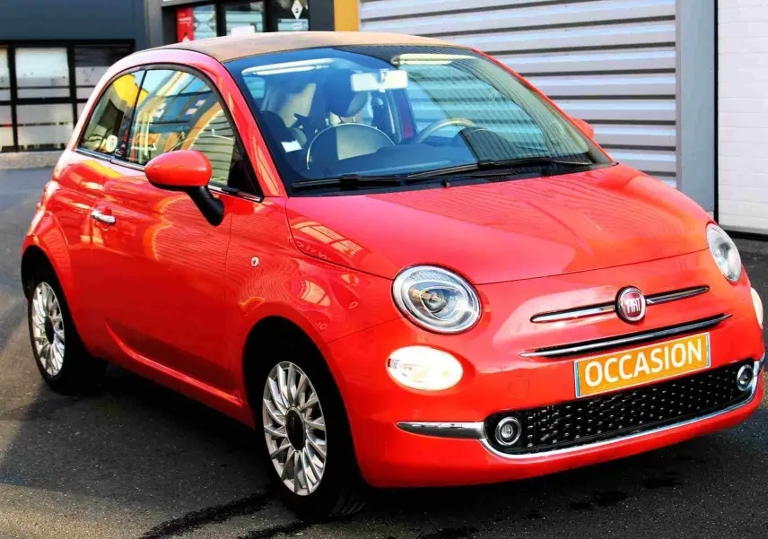 Gros plan sur la roue avant gauche d'une FIAT 500C 2018 en rouge pastel, avec jante argentée à rayons fins.