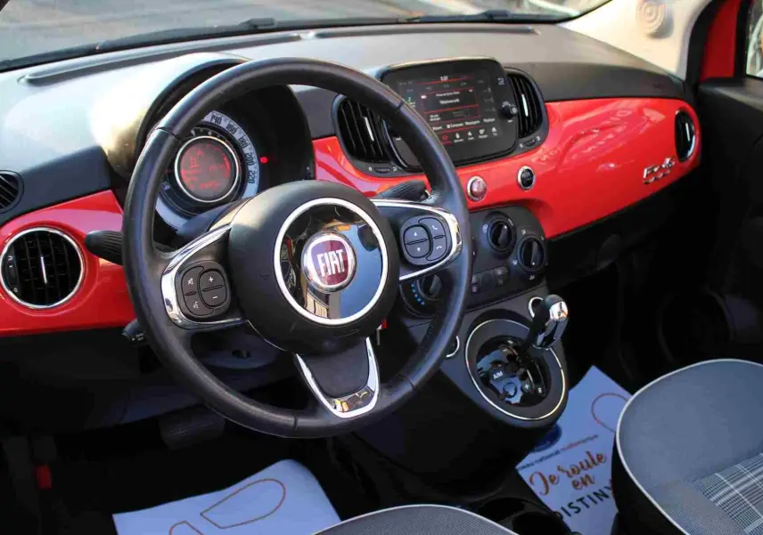 Vue intérieure côté conducteur du tableau de bord rouge pastel et des sièges gris à motifs de la Fiat 500C 2018.