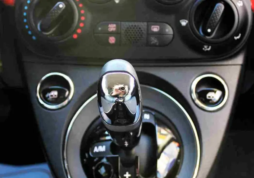 Gros plan sur le levier de vitesses automatique et les commandes de climatisation d’une FIAT 500C Pastel Coral Red de 2018.