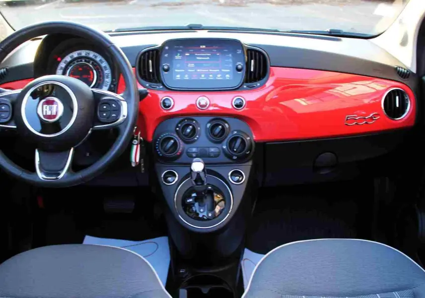 Vue intérieure avant du tableau de bord rouge pastel coral de la Fiat 500C 2018 avec volant multifonction et écran tactile central.