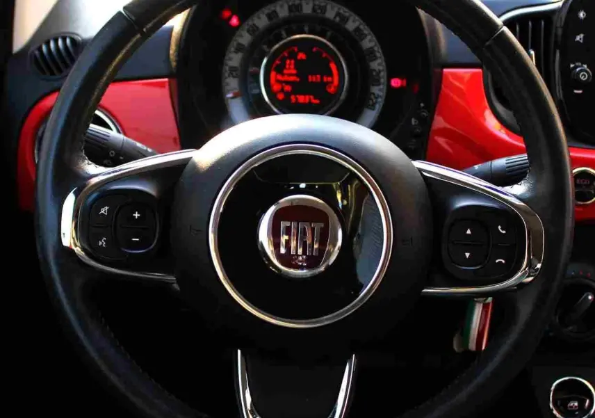 Vue intérieure centrée sur le volant noir de la Fiat 500C 2018 avec tableau de bord et inserts Pastel Coral Red.