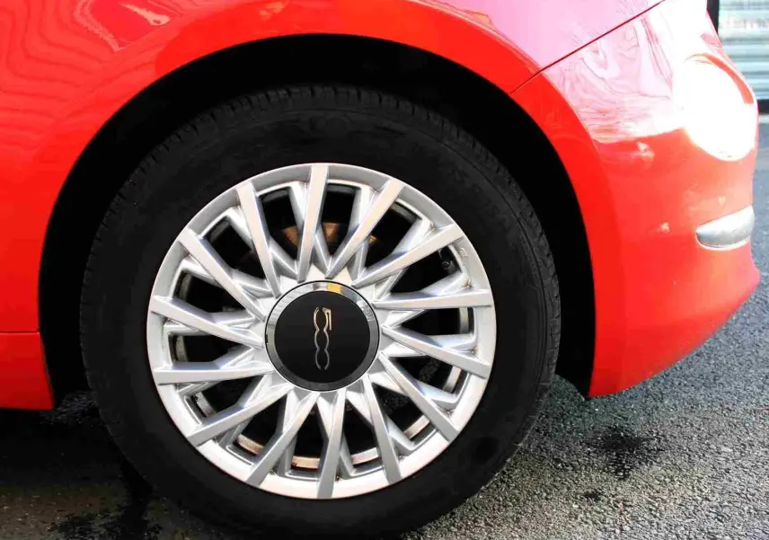 Gros plan sur la roue avant droite d'une FIAT 500C 2018 en rouge Pastel Coral avec jante argentée à rayons fins.