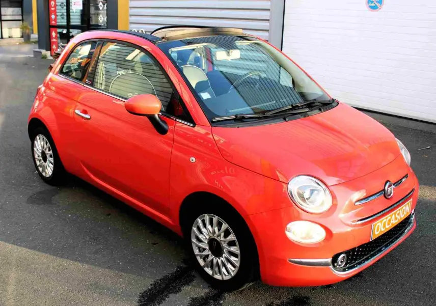 Gros plan sur la poignée intérieure chromée et les commandes de vitre côté gauche de la porte d'une Fiat 500C rouge corail.