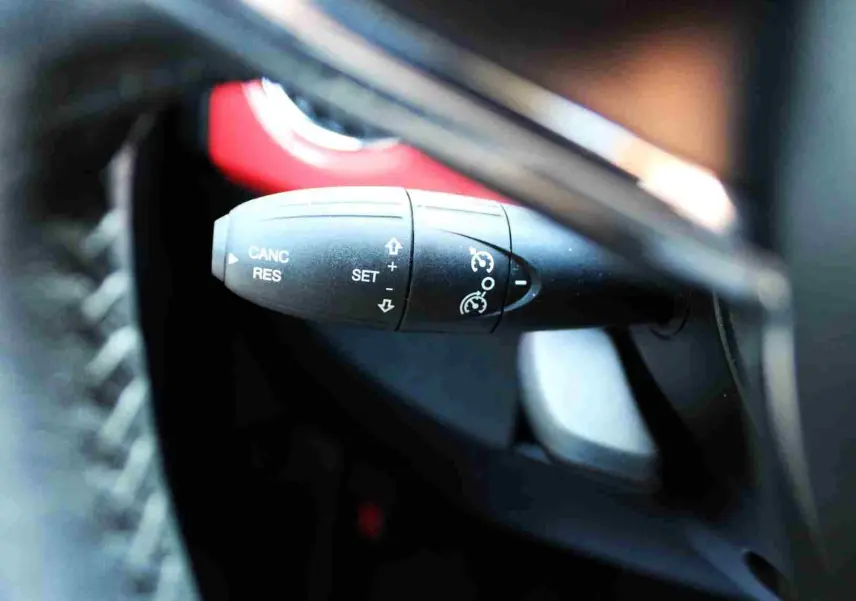 Gros plan sur la commande de régulateur de vitesse à gauche du volant d'une Fiat 500C 2018 rouge corail pastel.