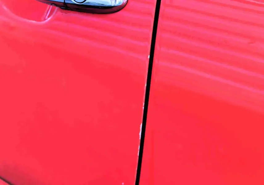 Détail du côté gauche de la porte avant d'une FIAT 500C 2018 en rouge pastel corail, avec reflet de lumière.