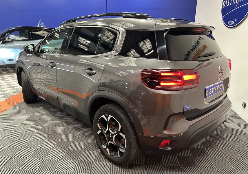 Vue 3/4 arrière droite d’un Citroën C5 Aircross gris Platinium avec feux arrière allumés en intérieur showroom.