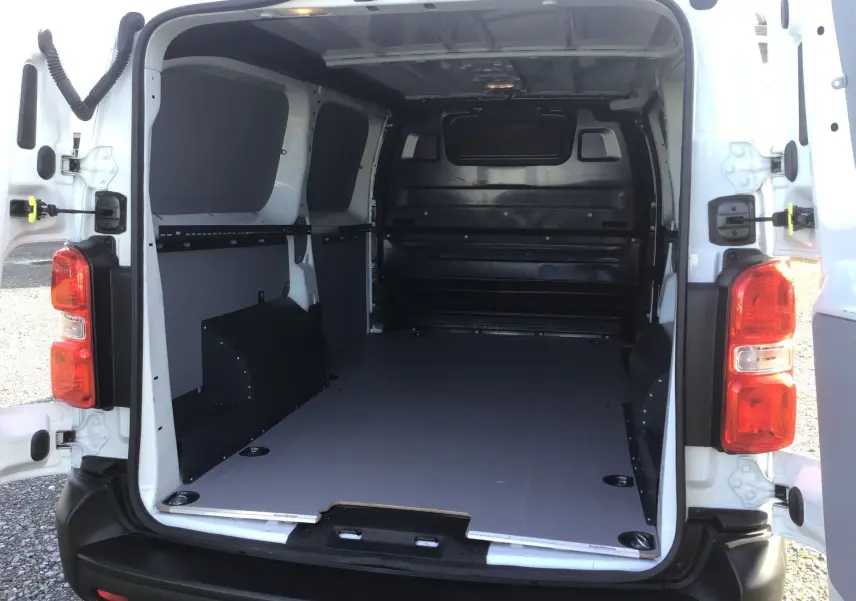 Vue arrière du fourgon blanc FIAT Scudo XL 2024, portes ouvertes montrant l’espace de chargement aménagé avec protection intérieure noire.