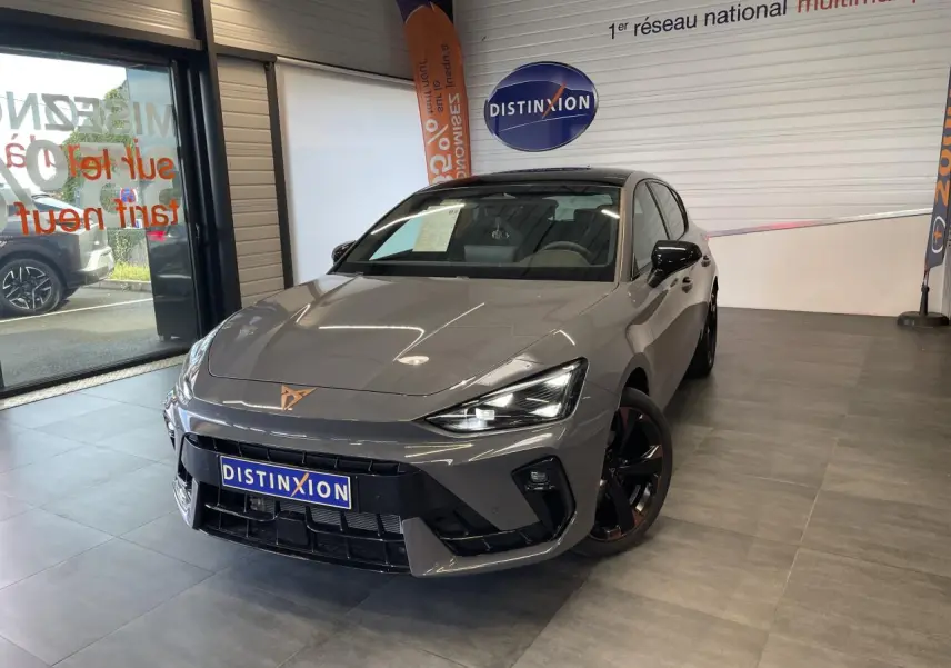 Vue 3/4 avant d'une CUPRA Leon gris magnétique avec jantes cuivrées et logo CUPRA sur le capot, en showroom.