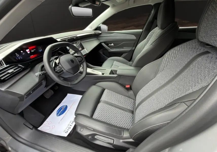Intérieur de la Peugeot 308 Hybrid 145 e-DCS6 Allure, vue côté conducteur, sièges gris tissu et cuir, tableau de bord moderne.