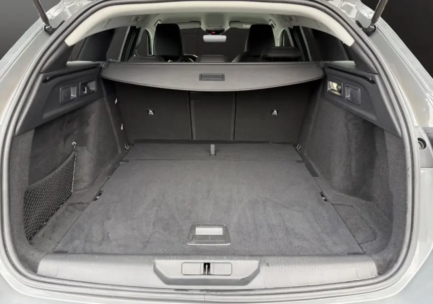 Coffre ouvert vu de l'arrière d'une Peugeot 308 Hybrid 145 gris foncé avec plancher plat et cache-bagages.