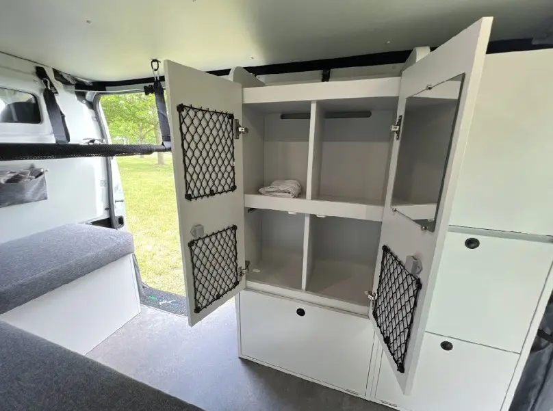 Vue intérieure du fourgon Renault Trafic gris, montrant un meuble de rangement blanc ouvert avec filets noirs sur les portes.