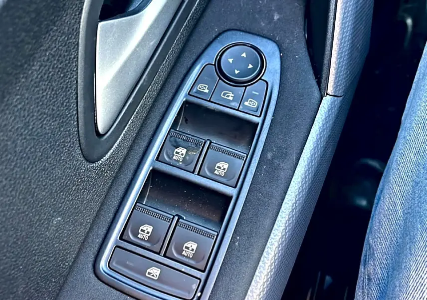 Gros plan sur les commandes de lève-vitres et rétroviseurs électriques côté conducteur du Dacia Duster noir 2026.