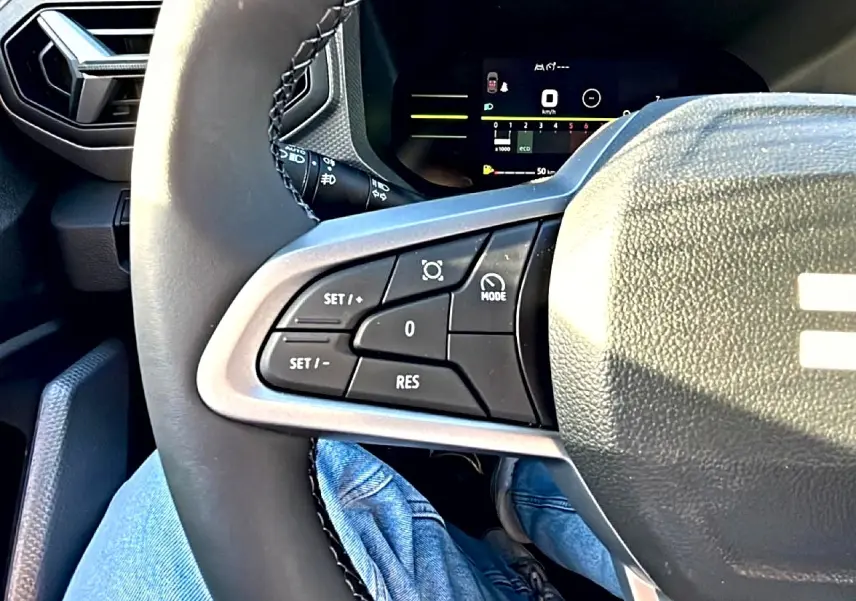 Gros plan sur les commandes multifonctions à gauche du volant noir du Dacia Duster 2026, avec tableau de bord digital en arrière-plan.